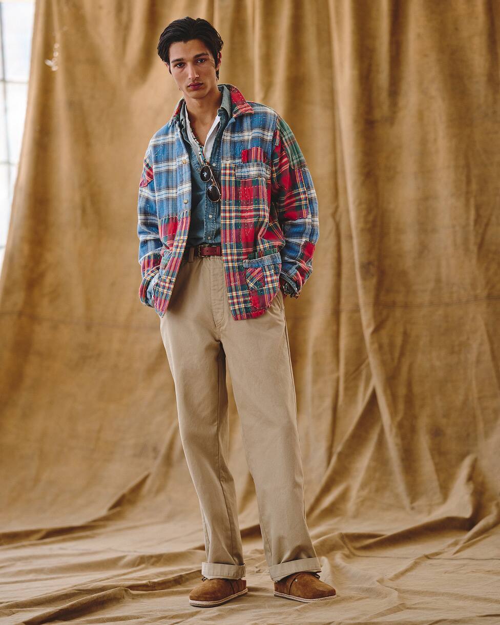 Man wearing a flannel shirt layered over a denim shirt, with beige trousers and loafers.