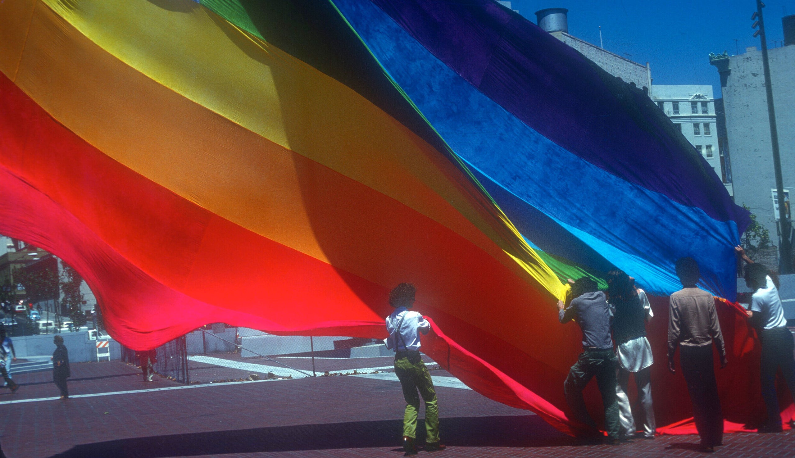 Gilbert Baker junto a varios voluntarios alzando la bandera del arcoíris original en la United Nations Plaza de San Francisco en 1978